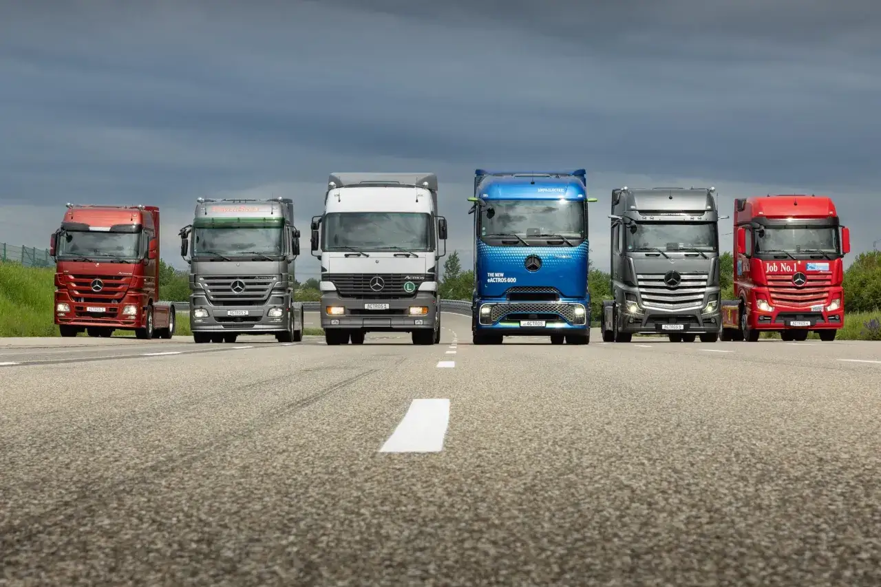 Six camions de la marque Mercedes-Benz, de différentes couleurs, alignés sur une route. Le camion bleu est 100% électrique.