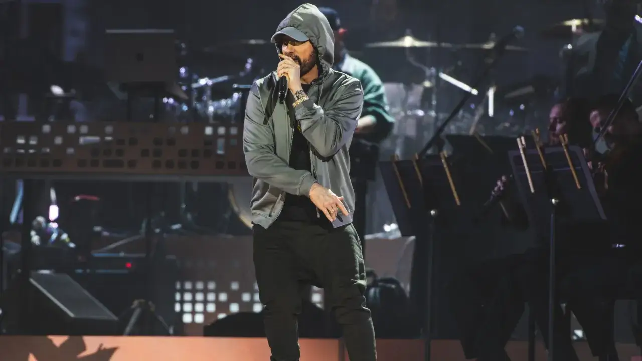 Eminem na scenie, w bluzie z kapturem, śpiewa do mikrofonu. Plotki o tym, że Eminem kiedyś zmarł, są nieprawdziwe.