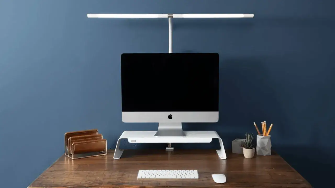 A sleek monitor setup with a light bar above, providing the best lighting for video conferencing. A minimalist desk with a keyboard, mouse, and organizer.