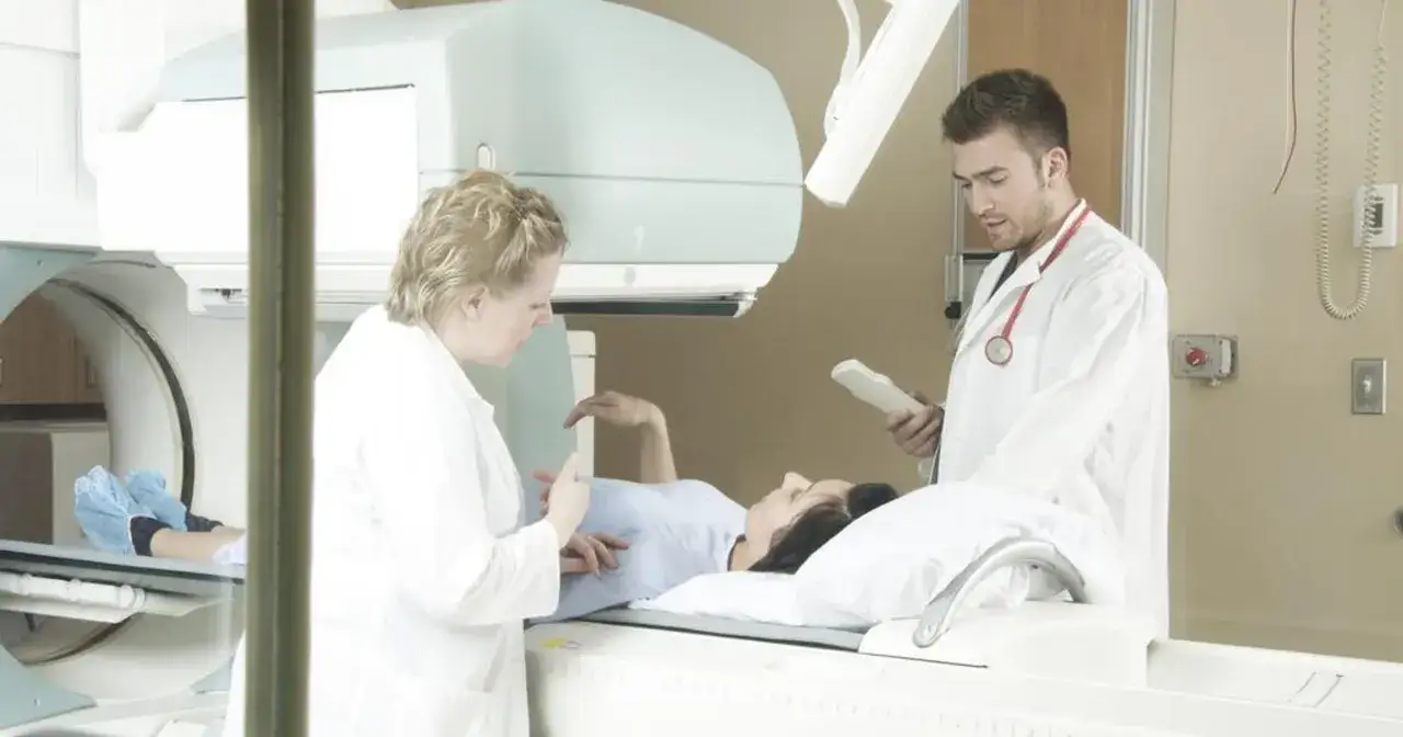 Pacjentka leży na stole zabiegowym, przygotowywana do radioterapii. Personel medyczny czuwa, by wszystko przebiegło sprawnie. Co gorsze chemioterapia czy radioterapia?