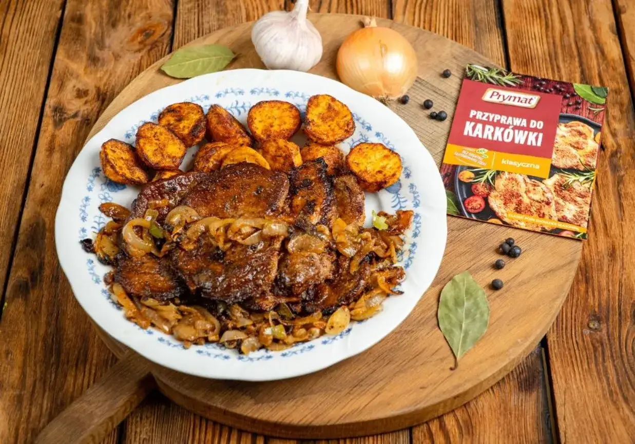 Pyszny karczek z piekarnika z pieczonymi ziemniakami i cebulką. Obok leży przyprawa do kark&oacute;wki Prymat.