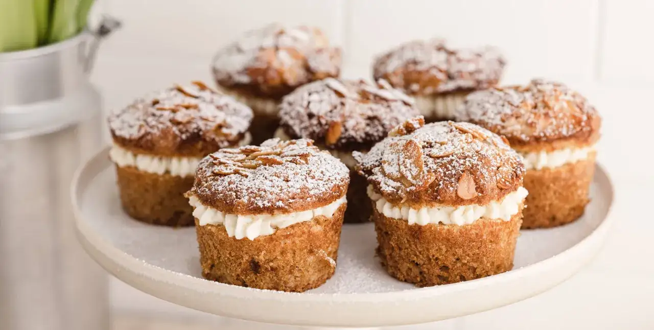 Sieben bienenstich muffins mit einer cremigen F&uuml;llung und Mandelsplittern, best&auml;ubt mit Puderzucker.