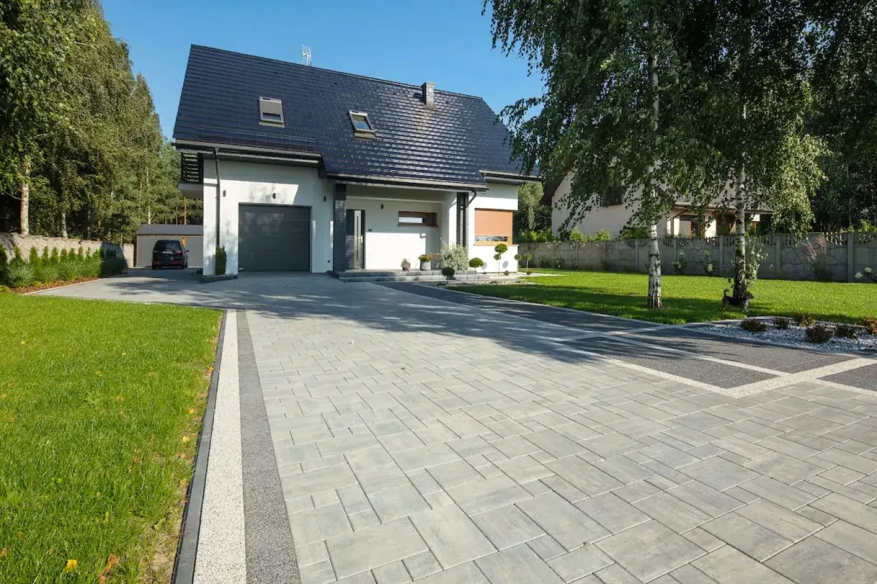 Nowy, nowoczesny dom z podjazdem z kostki brukowej. Chodnik od furtki do domu prowadzi przez zadbany ogród.