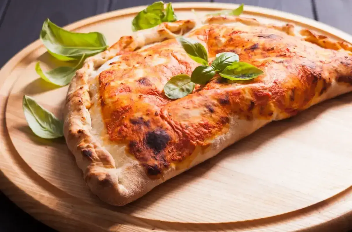 Złocisty calzone z sosem pomidorowym i serem, ozdobiony listkami bazylii. Pyszna przekąska, kt&oacute;rej **calzone kcal** nie są aż tak straszne.