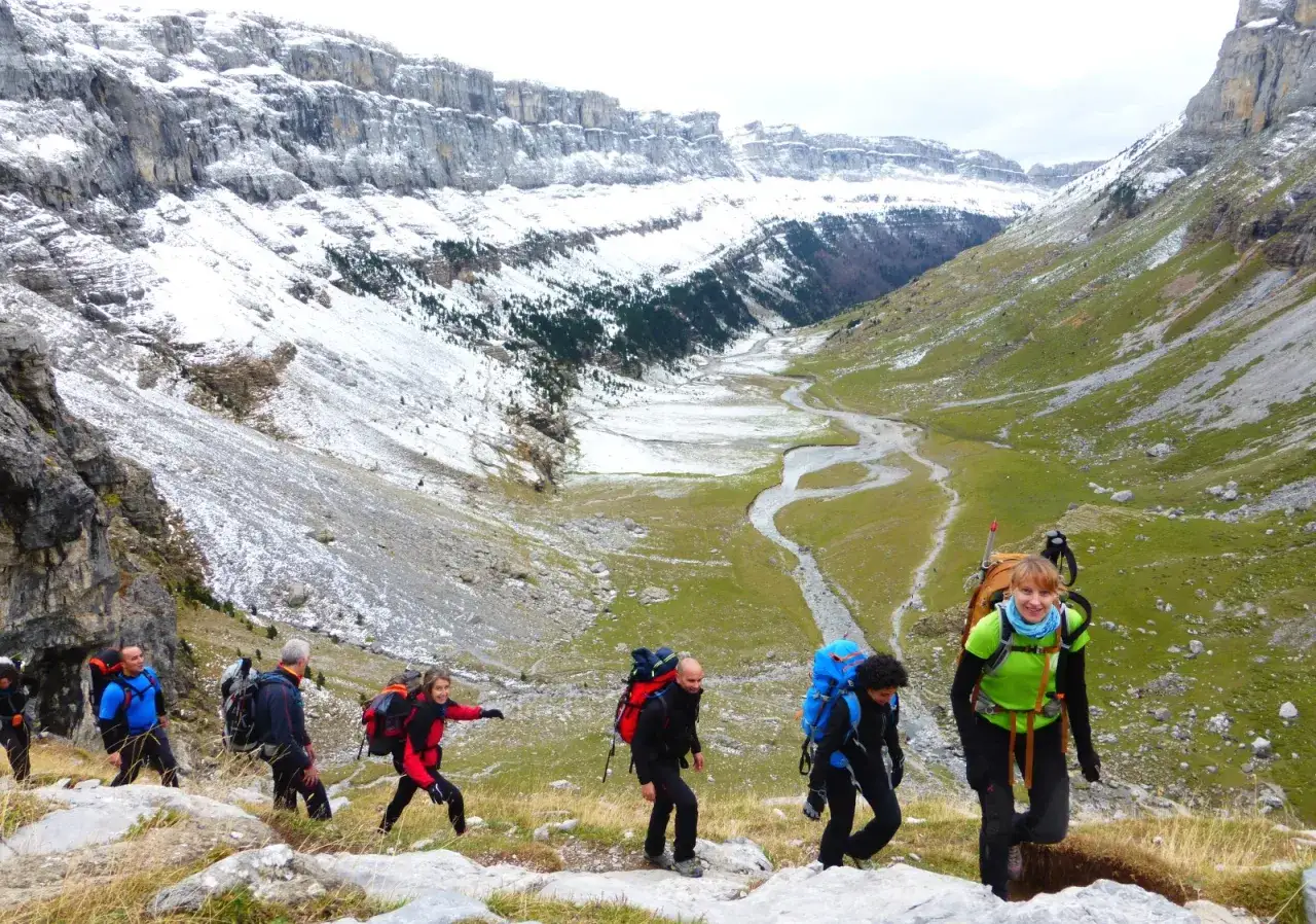 Senderismo en el valle de Ordesa, Monte Perdido Huesca. Montañeros con mochilas ascienden por un sendero rocoso con nieve en las laderas.