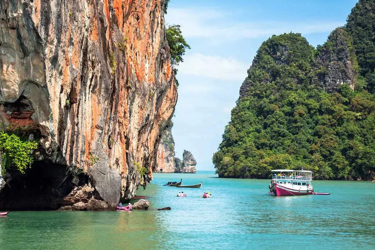 Klippor och gröna berg reser sig ur turkost vatten vid Khao Lak. Båtar och kajaker syns i det klara vattnet.