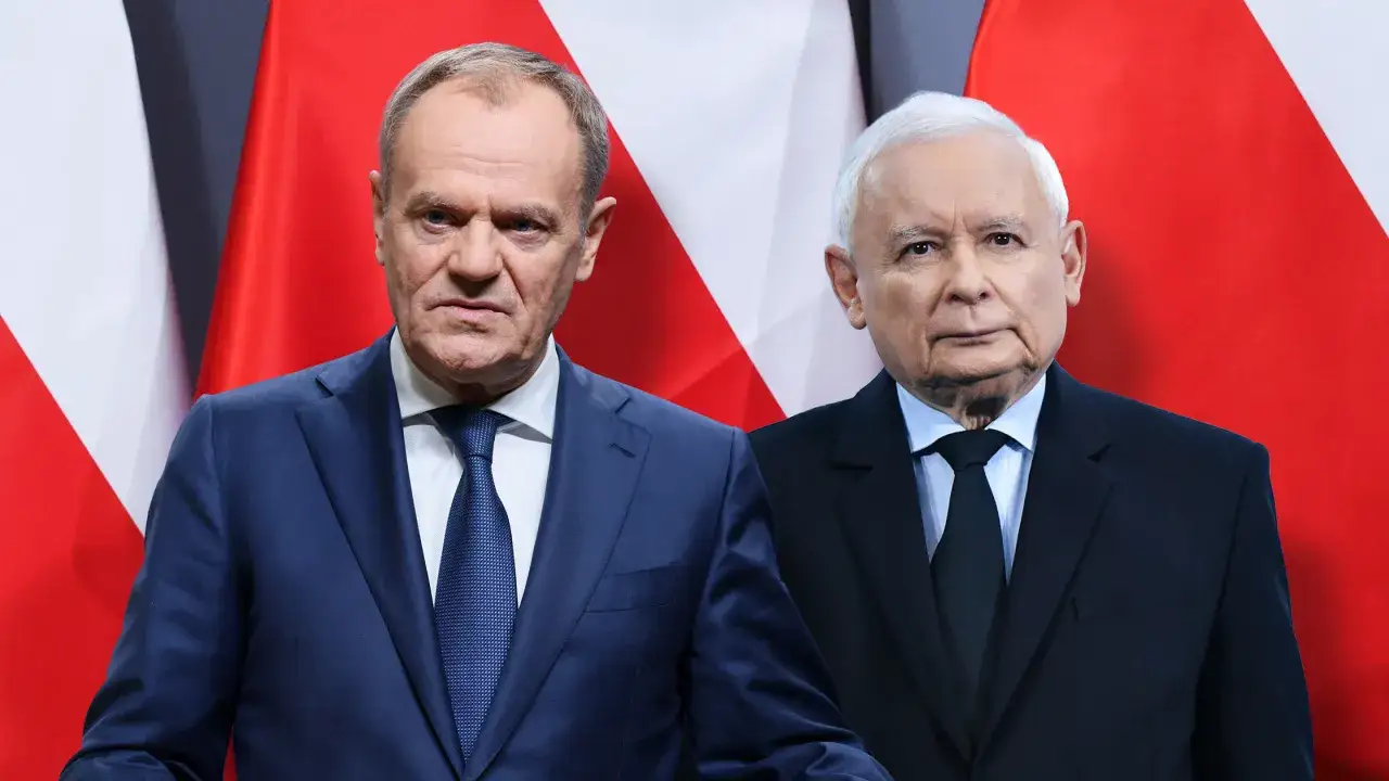 Dwóch polityków na tle flagi Polski. Czy Tusk jest rudy? Nie, jego włosy są w odcieniu blond.