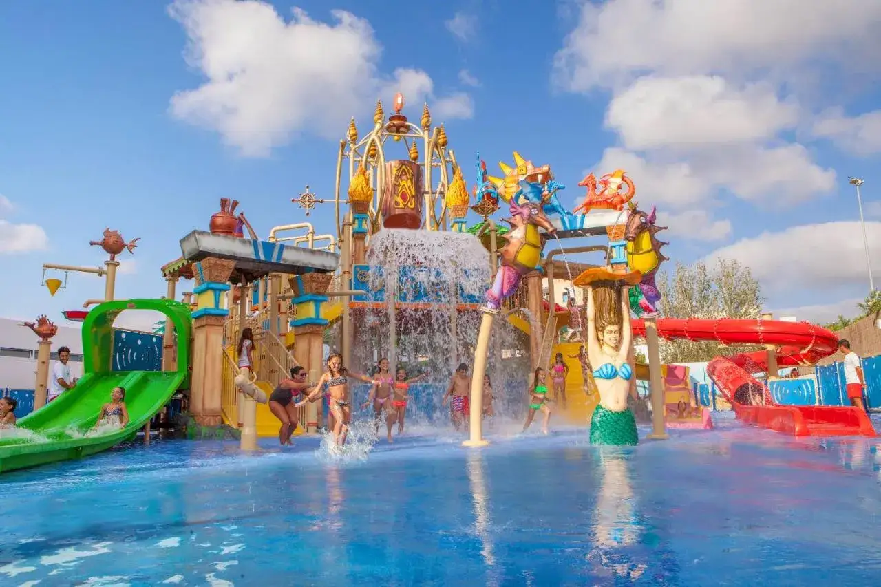 Niños disfrutan de piscinas con toboganes, cascadas y figuras de sirenas en un día soleado.