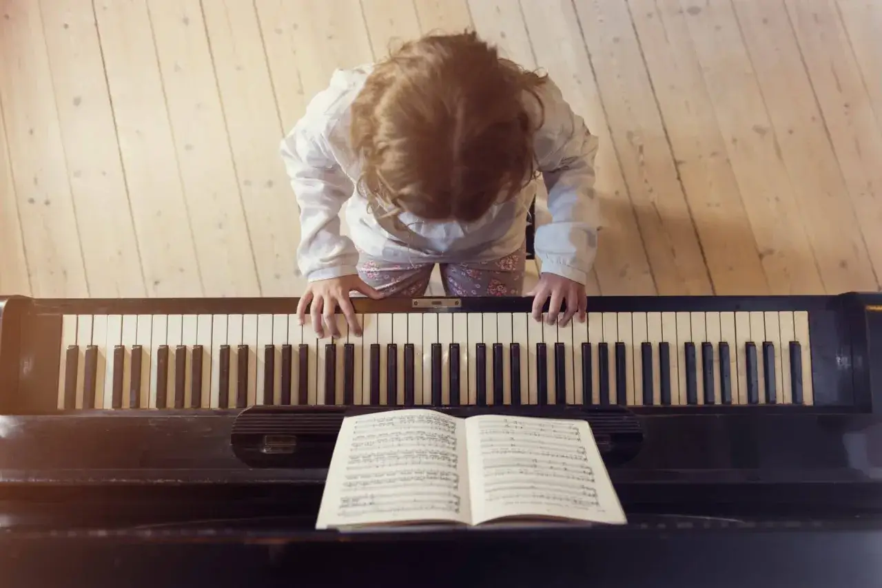 Une petite fille apprend à jouer d'un instrument, ses doigts effleurant les touches du piano.