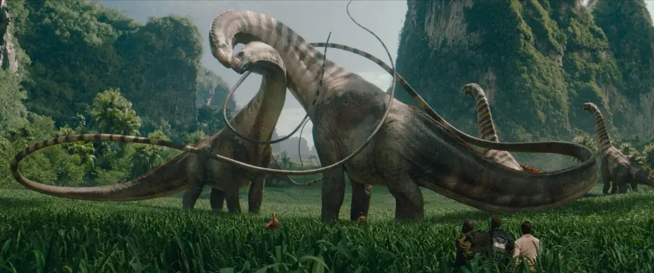 I en grönskande dalgång, likt ett **nya jurassic park**, betar flera långhalsade dinosaurier. I förgrunden skymtar tre personer som betraktar dem.