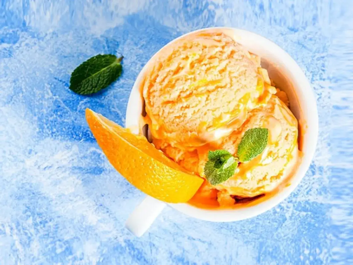 Erfrischendes orangen sorbet in einer Schale, garniert mit frischer Minze und einem Orangenfilet auf blauem Hintergrund.