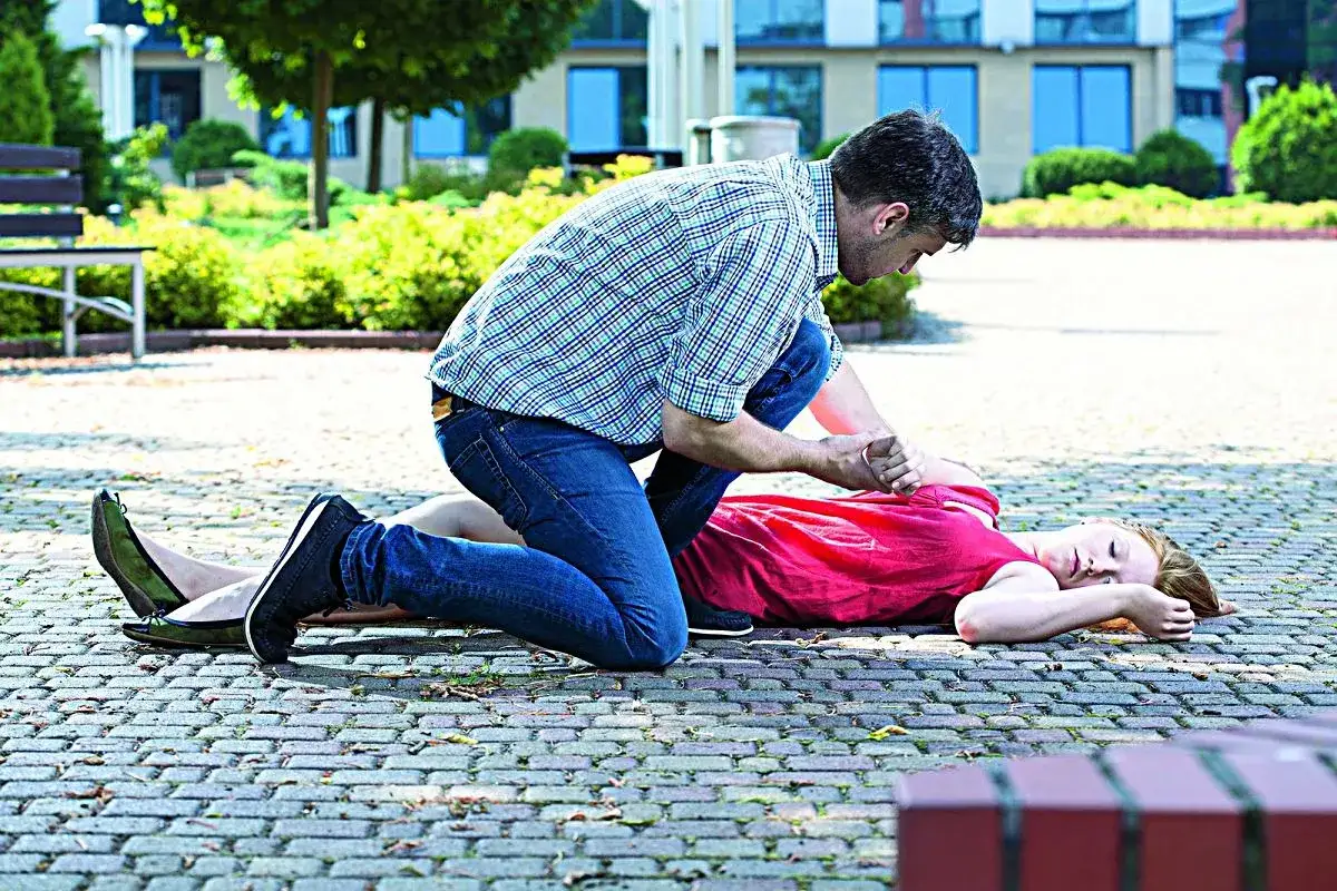 Mężczyzna klęczy przy kobiecie leżącej na ziemi, która doświadczyła omdlenia we śnie.