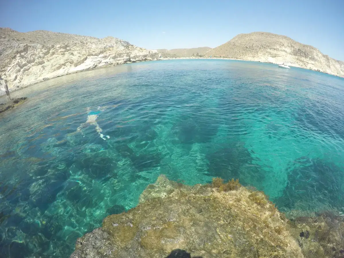 Aguas cristalinas en calas de agua amarga, con rocas y una persona nadando.