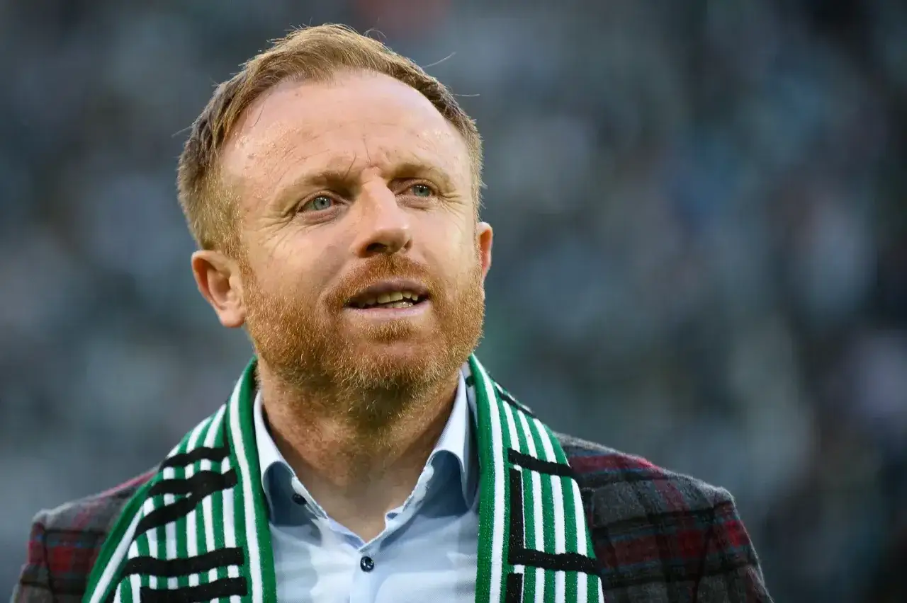 Piotr Stokowiec, trener w szaliku klubowym, z uwagą obserwuje boisko.