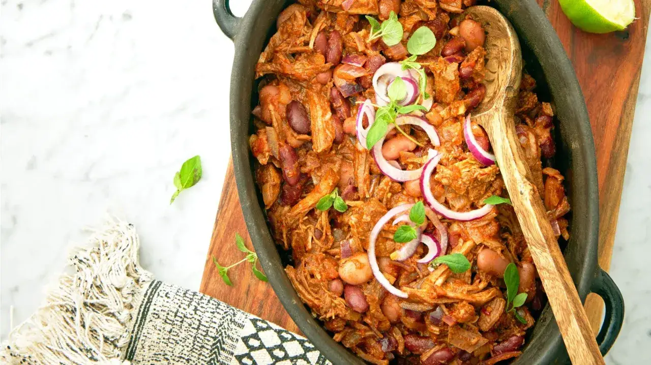 En mustig pulled pork gryta med b&ouml;nor och r&ouml;dl&ouml;k, redo att serveras med en tr&auml;sked.