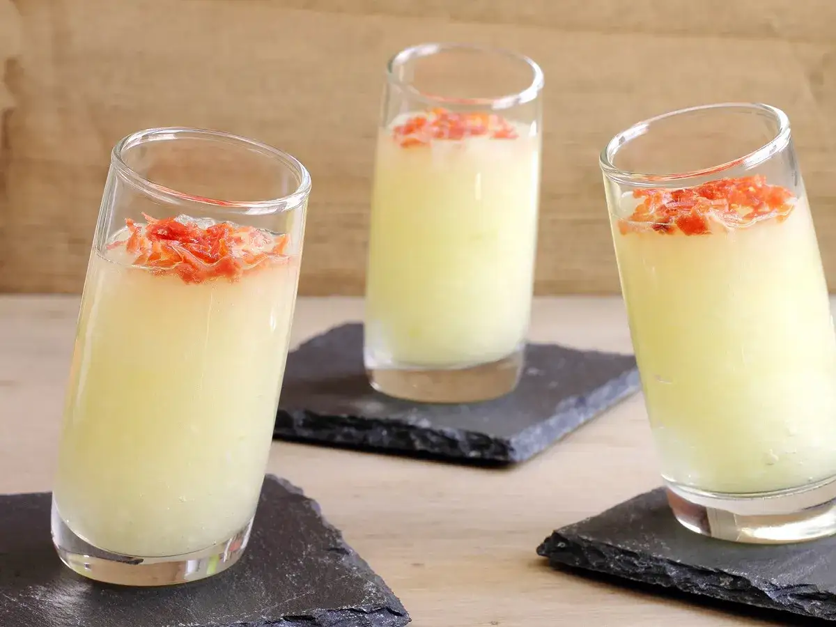Trois verres de soupe de melon glac&eacute;e, garnie de jambon cru effiloch&eacute;, servis sur des ardoises.