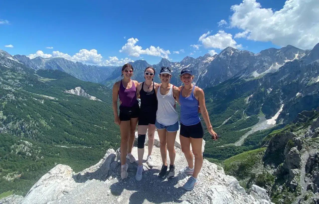 Vier Freundinnen genießen die atemberaubende Aussicht auf die albanischen Alpen. Ihr Abenteuer beim Backpacking in Albanien führt sie auf Gipfel mit grünen Tälern und schneebedeckten Bergen.