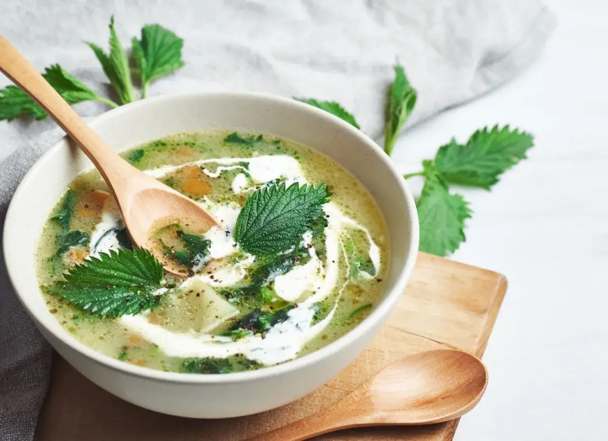 A creamy zupa z pokrzywy ozdobiona świeżymi liśćmi pokrzywy, podana w misce z drewnianą łyżką.