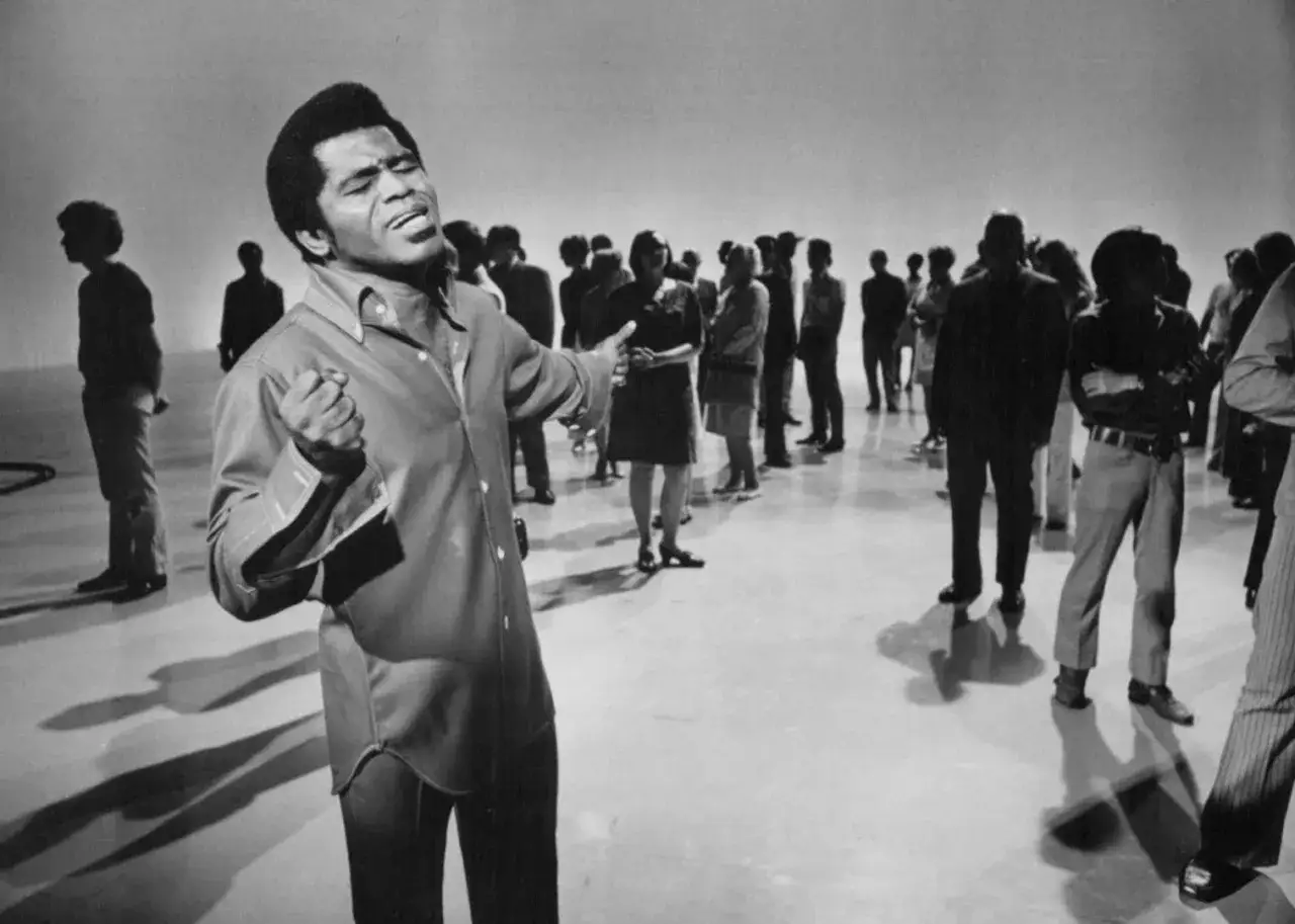 James Brown, król **soul** music, śpiewa z pasją, otoczony przez publiczność.