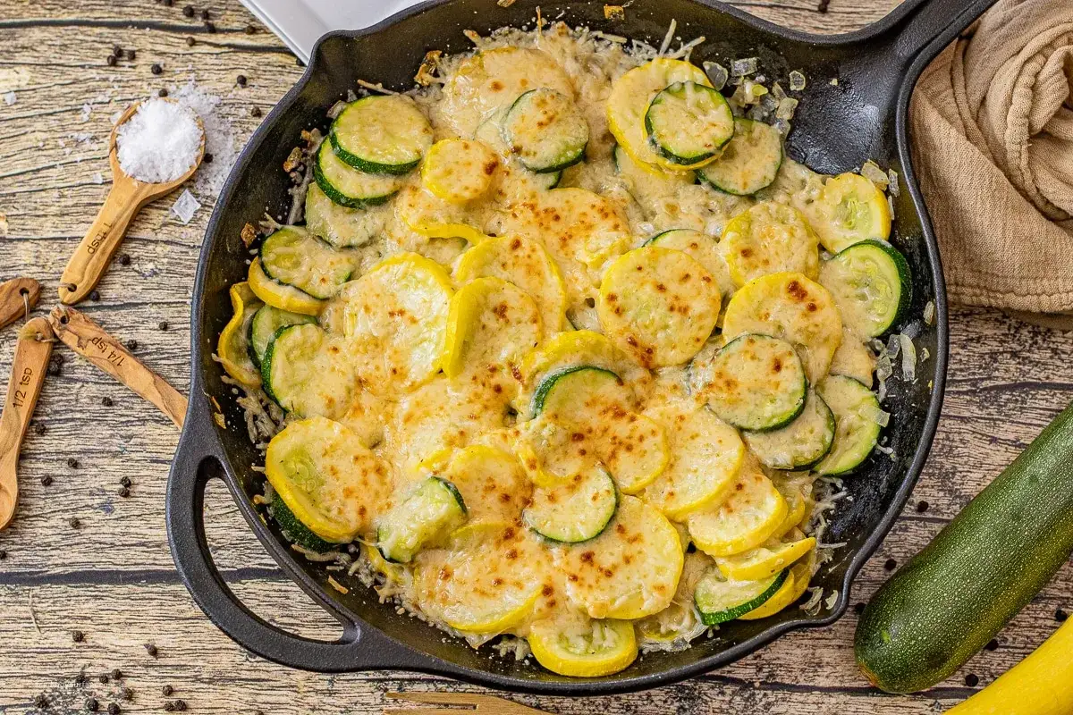 Gebackene gelbe Zucchini und gr&uuml;ne Zucchini mit geschmolzenem K&auml;se in einer Gusseisenpfanne, garniert mit Salz und Pfeffer.