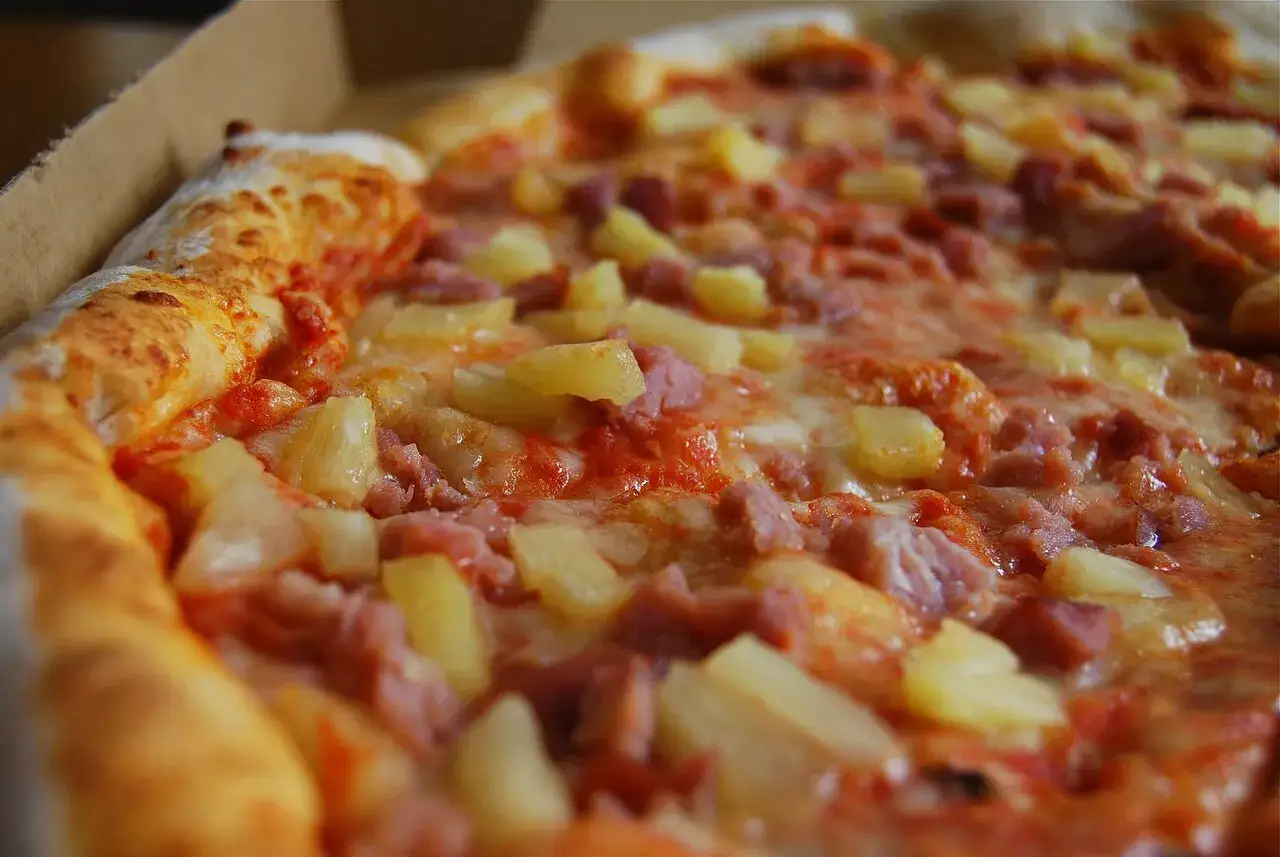 Pizza hawajska, której kto wymyślił, z ananasem i szynką, w pudełku.