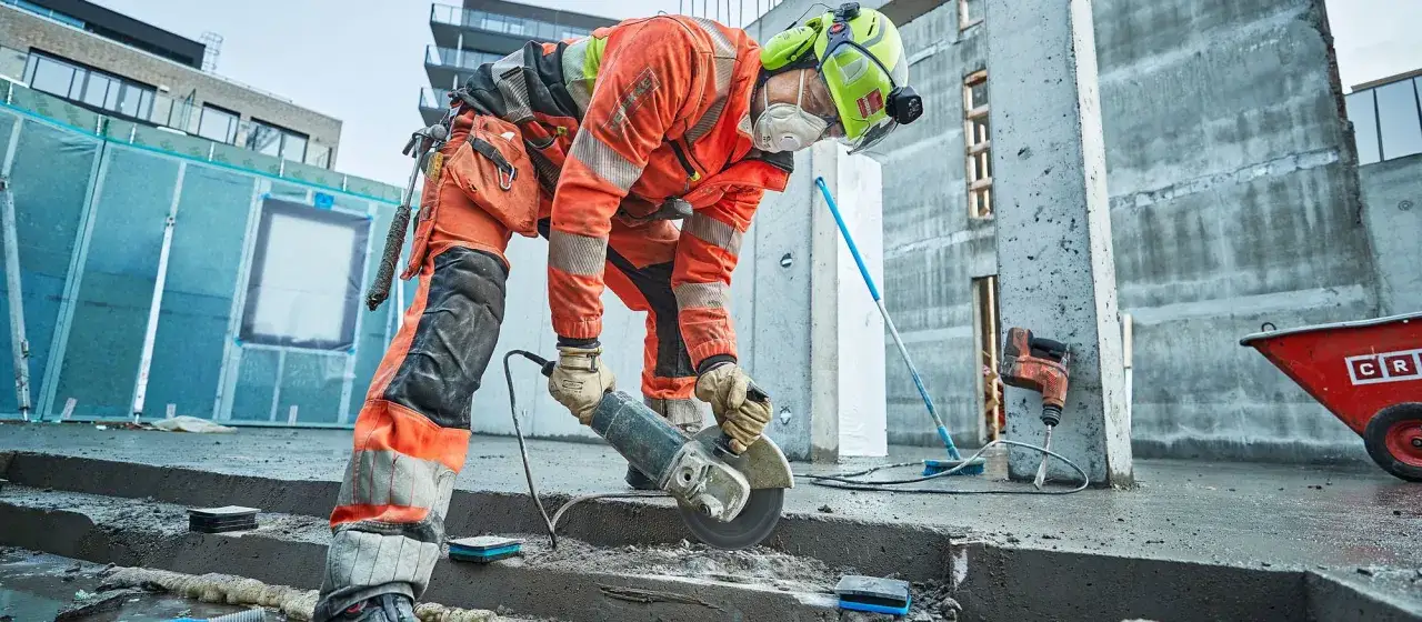 Byggarbetare med skyddsutrustning anv&auml;nder vinkelslip. Glasull kan vara farligt, s&aring; skydd &auml;r viktigt.