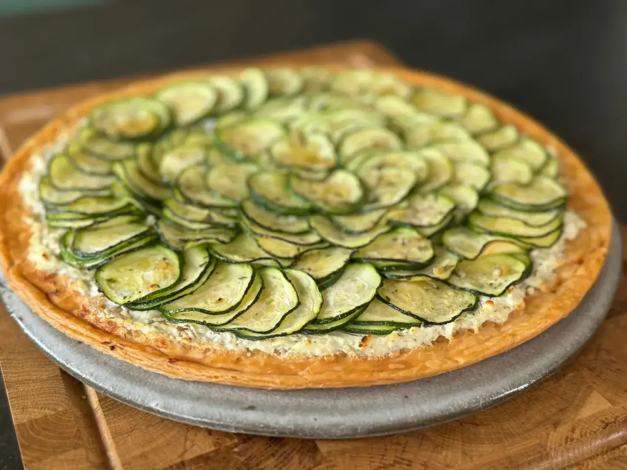 Tarte courgette aux fines rondelles de courgettes dispos&eacute;es en rosace sur une garniture cr&eacute;meuse, sur une p&acirc;te feuillet&eacute;e dor&eacute;e.