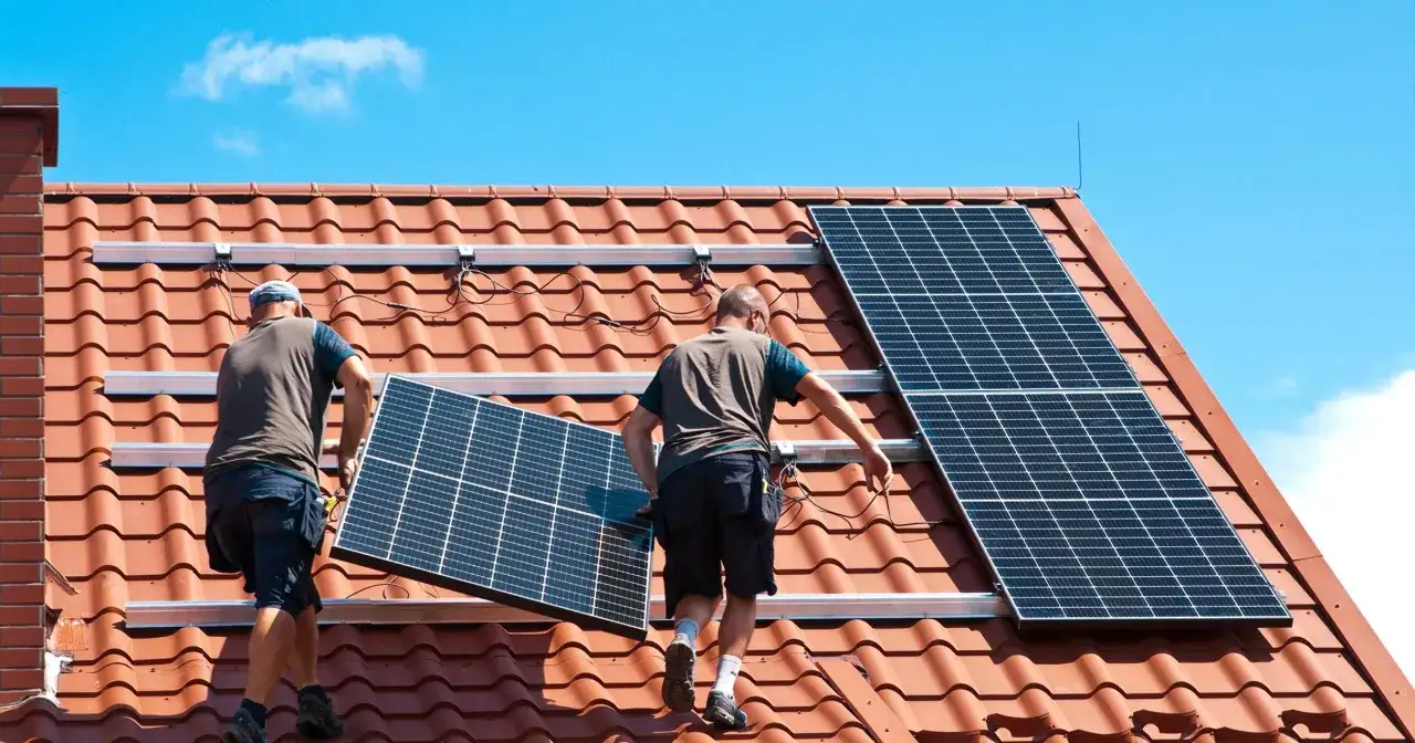 Dwóch mężczyzn montuje panele słoneczne na czerwonym dachu. Instalacja paneli słonecznych to krok w stronę ekologicznej energii.