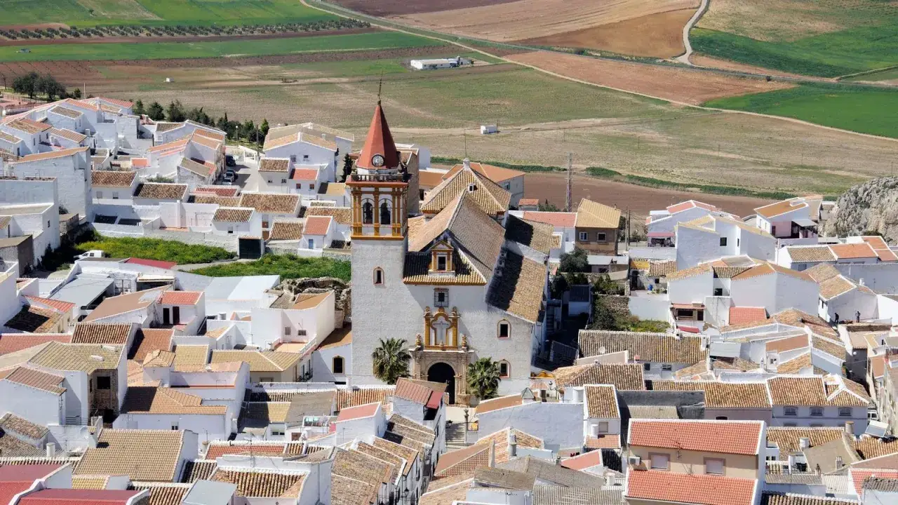 Vista aérea del pintoresco pueblo teba, con casas blancas y tejados de teja, dominado por una iglesia con campanario.