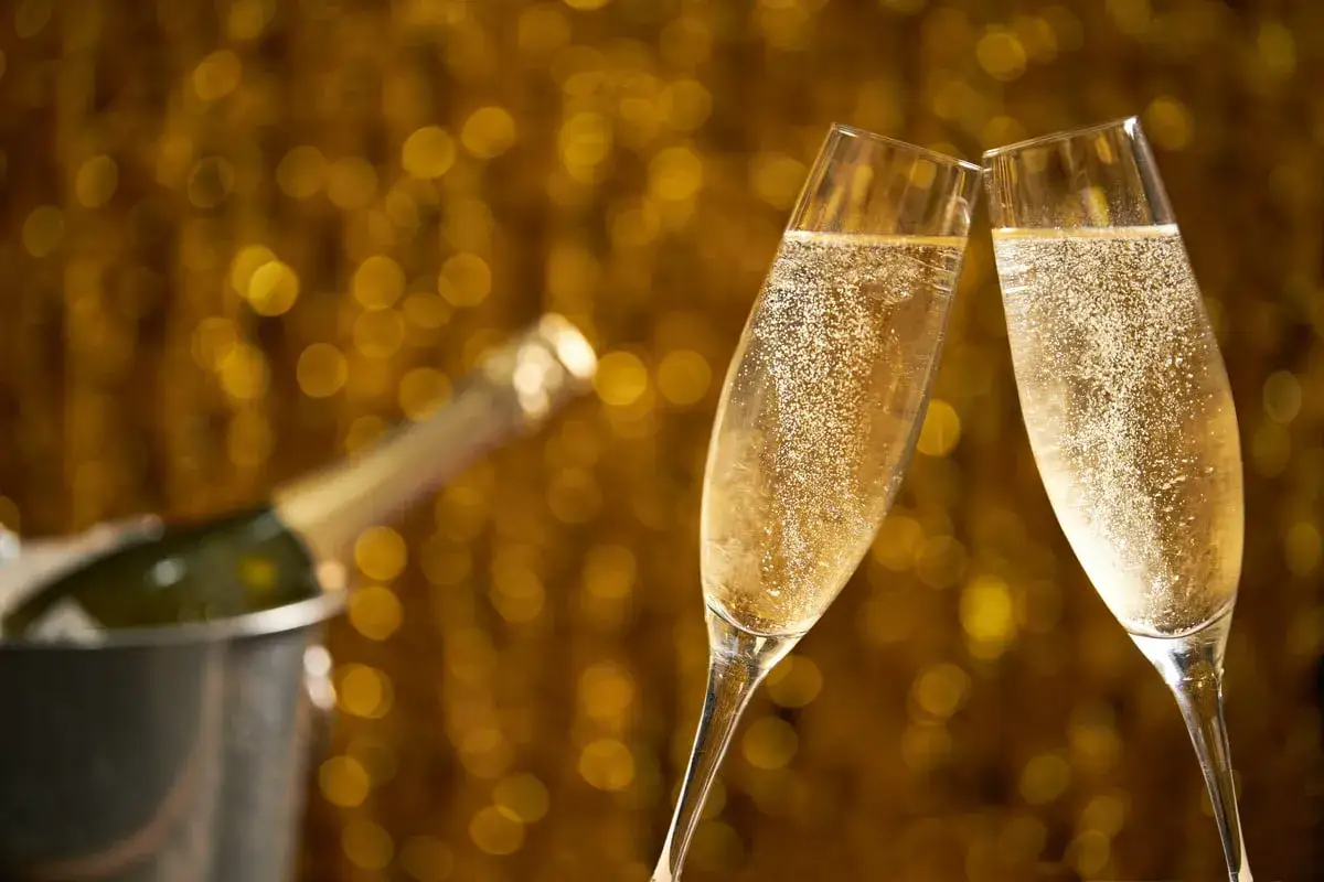Deux flûtes de champagne pétillant se touchent sur un fond doré scintillant. Une bouteille est au frais dans un seau à glace. C'est le moment de boire du champagne !
