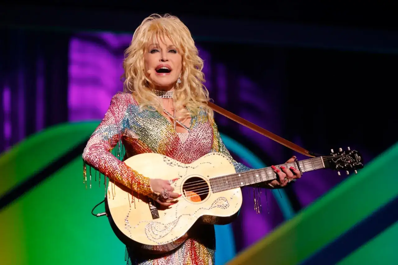 Dolly Parton, die legend&auml;re Country-S&auml;ngerin, spielt Gitarre in einem schillernden Regenbogen-Outfit. Sie sieht aus, als w&auml;re sie nie &auml;lter geworden, und man fragt sich, wie alt ist Dolly Parton wirklich?
