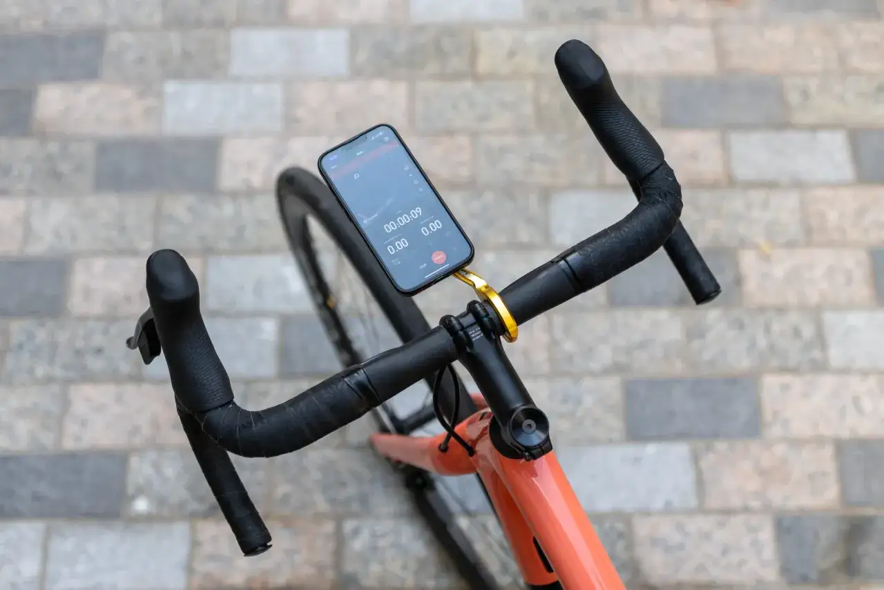 Na kierownicy roweru zamontowano smartfon, który służy jako licznik. Wyświetla czas jazdy 00:00:09 i dystans 0.00 km.
