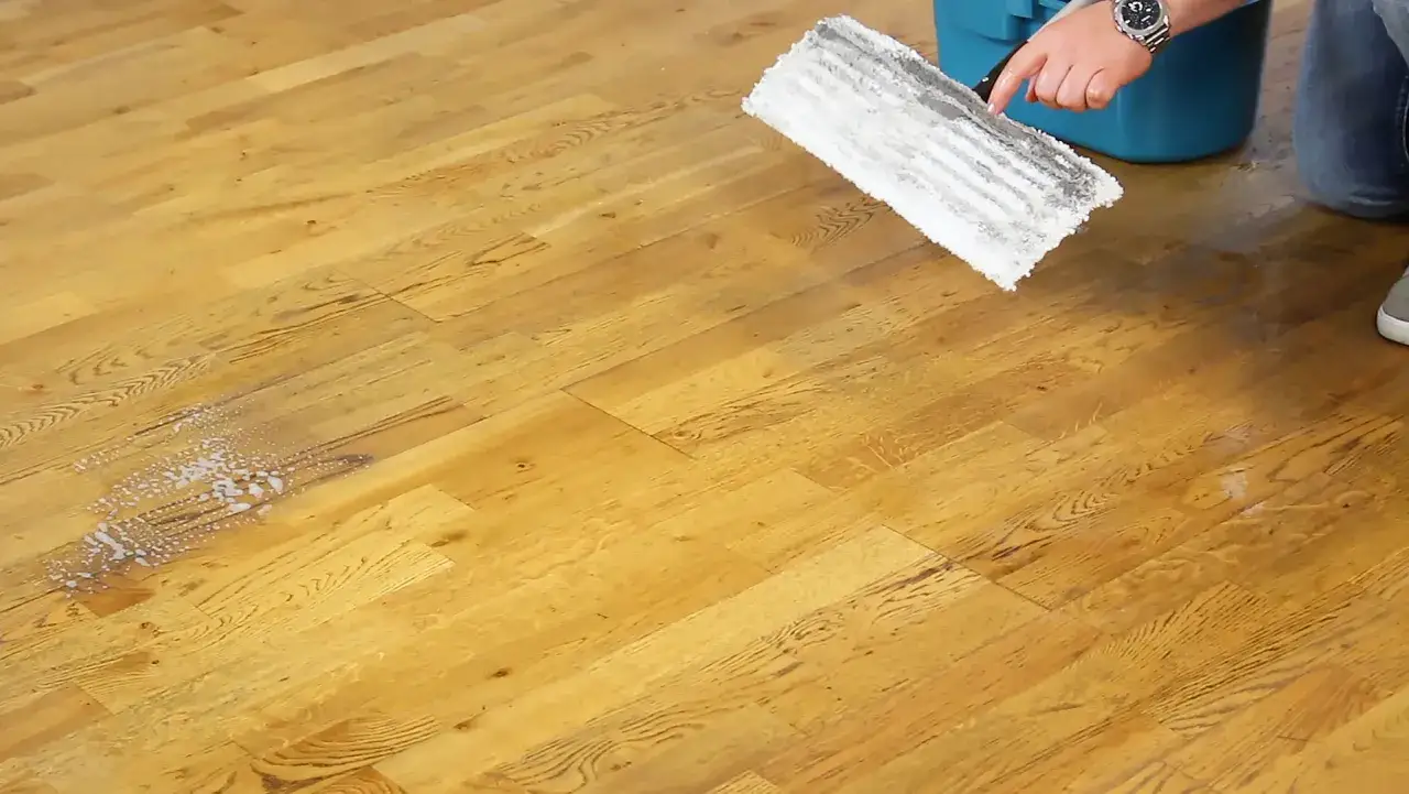 Ein Mann reinigt einen Holzboden mit einem Mopp. Die **Parkett Pflege** wird mit einem Reinigungsmittel durchgef&uuml;hrt, das Schaum hinterl&auml;sst.