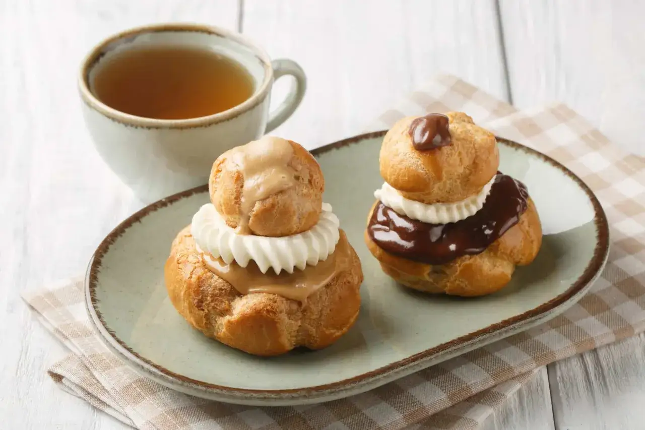 Deux religieuses, l'une au chocolat, l'autre &agrave; la cr&egrave;me, sur une assiette avec une tasse de th&eacute;.