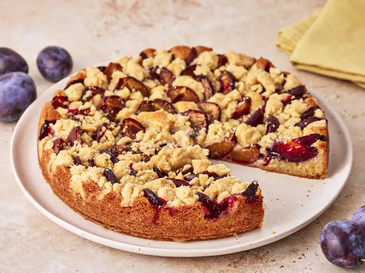 Saftiger Pflaumenkuchen mit Streuseln, gebacken in einer Springform. Ein Stück fehlt bereits, was Appetit macht.