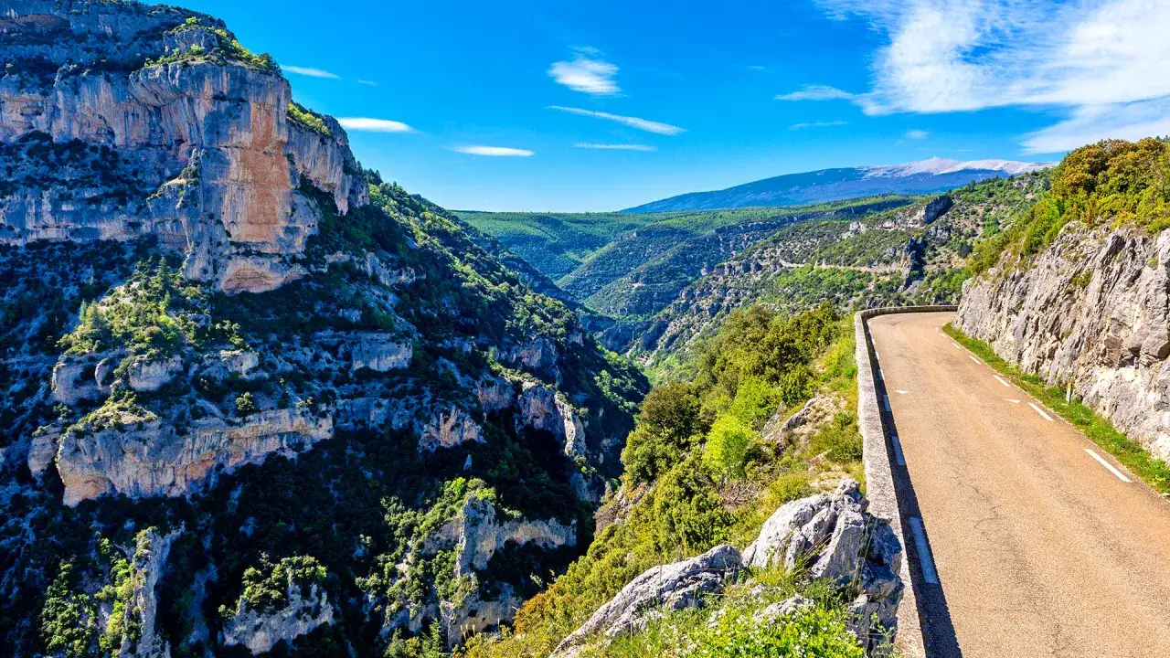 Route sinueuse traversant les gorges de la Nesque, offrant des vues spectaculaires sur les falaises et la vallée verdoyante.