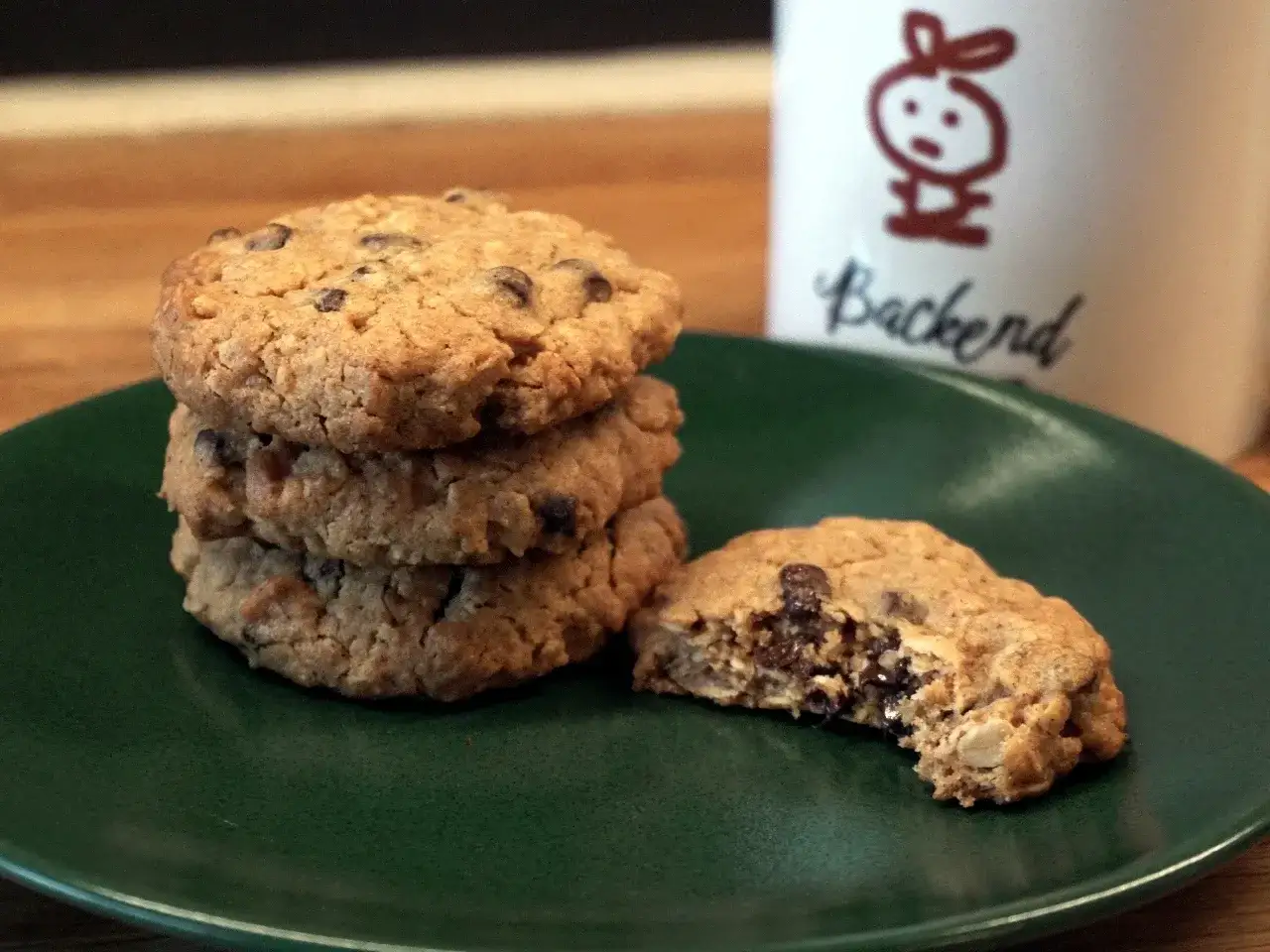 En h&ouml;g med gammaldags havrekakor med chokladbitar p&aring; en gr&ouml;n tallrik. En kaka &auml;r upp&auml;ten. En mugg med en kaninfigur och texten 