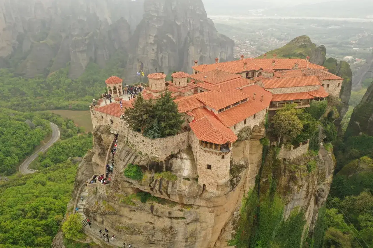 Climbing stairs to reach the Meteora monasteries perched on rocky cliffs. A winding road leads to this breathtaking view.