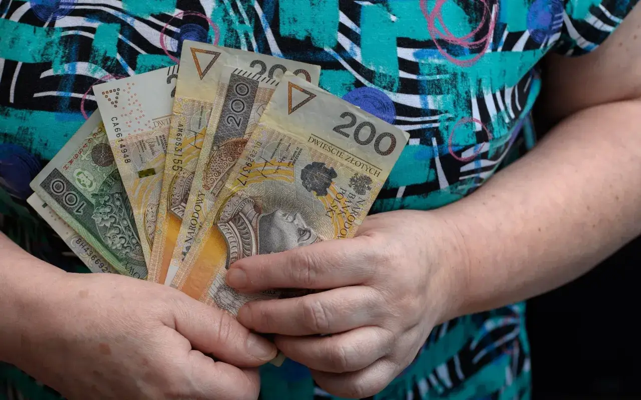 Dłonie trzymają polskie banknoty 100 i 200 zł. Pytanie: ile wynosi renta rodzinna po ojcu z KRUS?