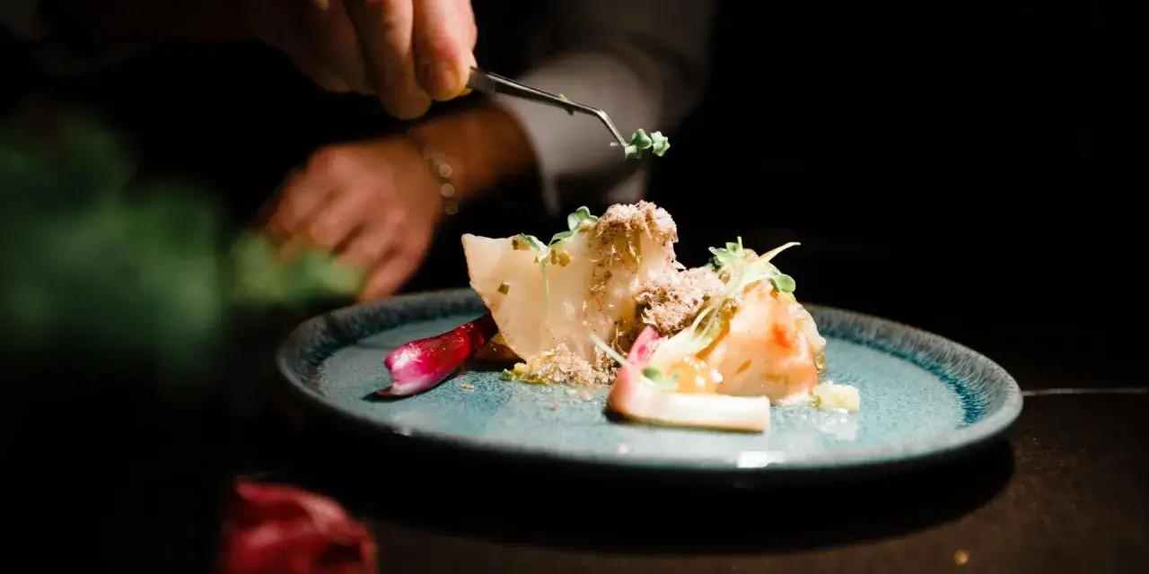 Un cuoco decora un piatto gourmet con erbe fresche, un'opera d'arte culinaria che evoca i sapori di Roanne, Francia.