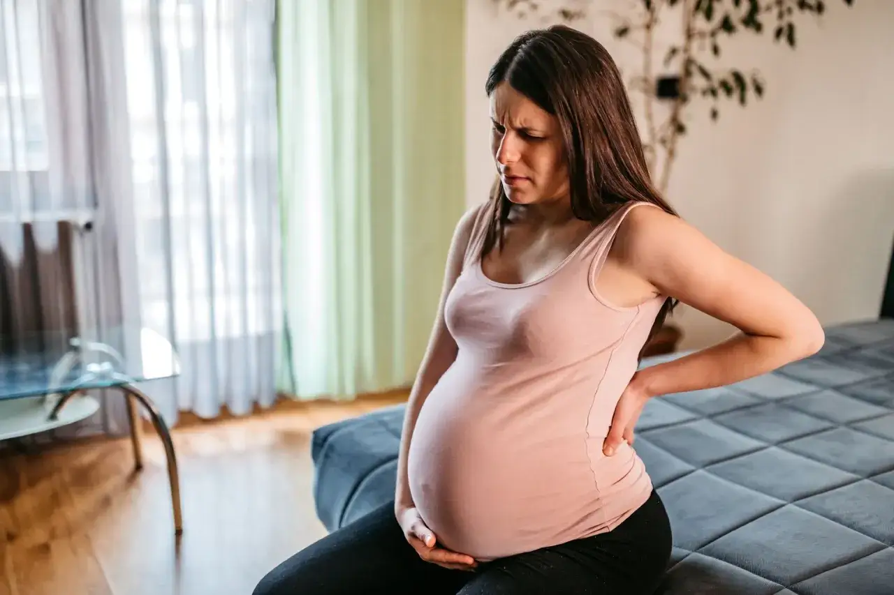 Schwangere Frau im 3. Trimester mit oberbauchschmerzen, h&auml;lt sich den R&uuml;cken.