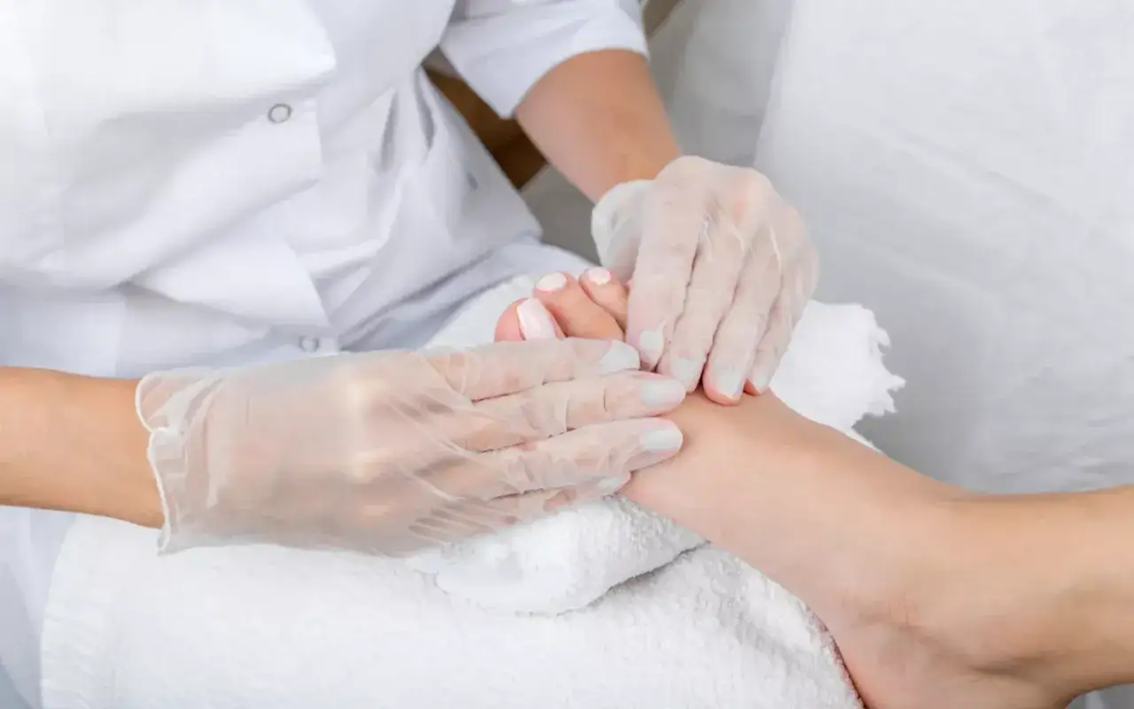 Mains gant&eacute;es prodiguant une prise en charge pedicure experte, avec soin des ongles et massage doux du pied sur une serviette blanche.