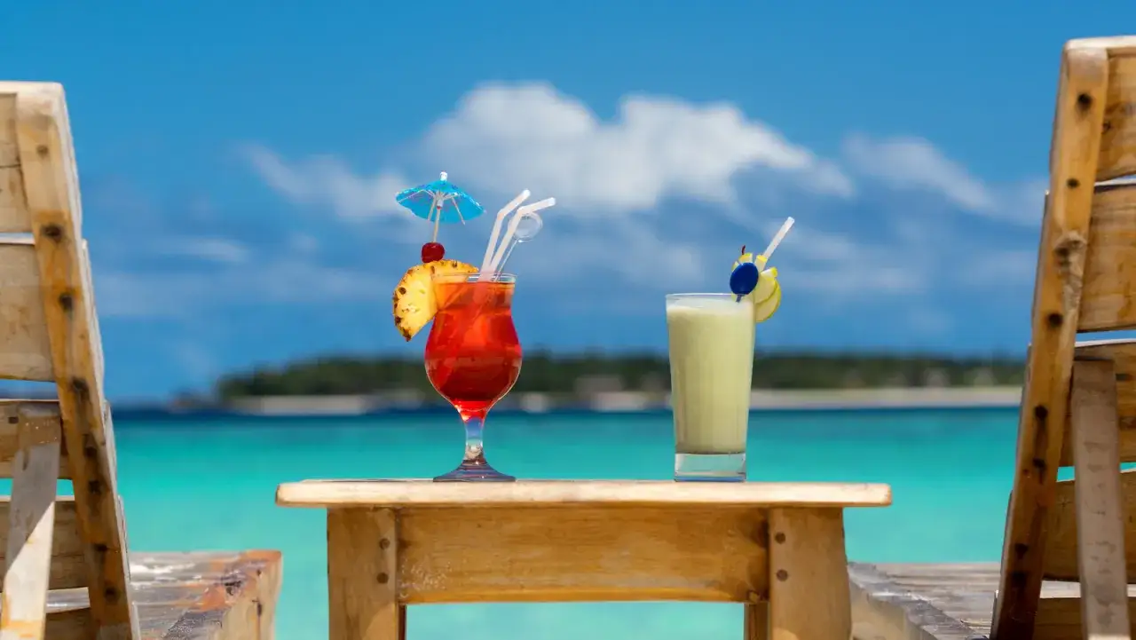Dwa drinki na plaży, jeden czerwony z ananasem i parasolką, drugi zielony. Idealne na przepis na sex on the beach.