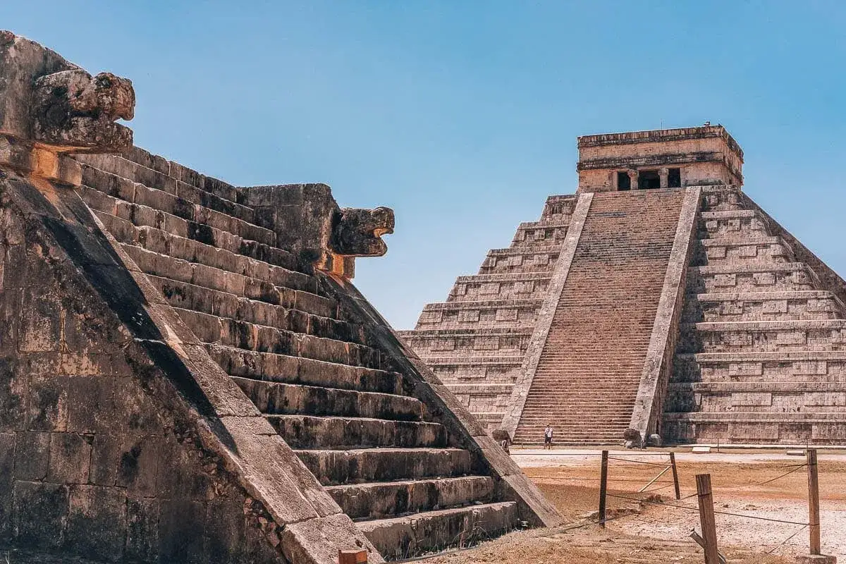 Kamienne piramidy w Chichen Itza, z kamiennymi wężami u podnóża schodów, pod błękitnym niebem.