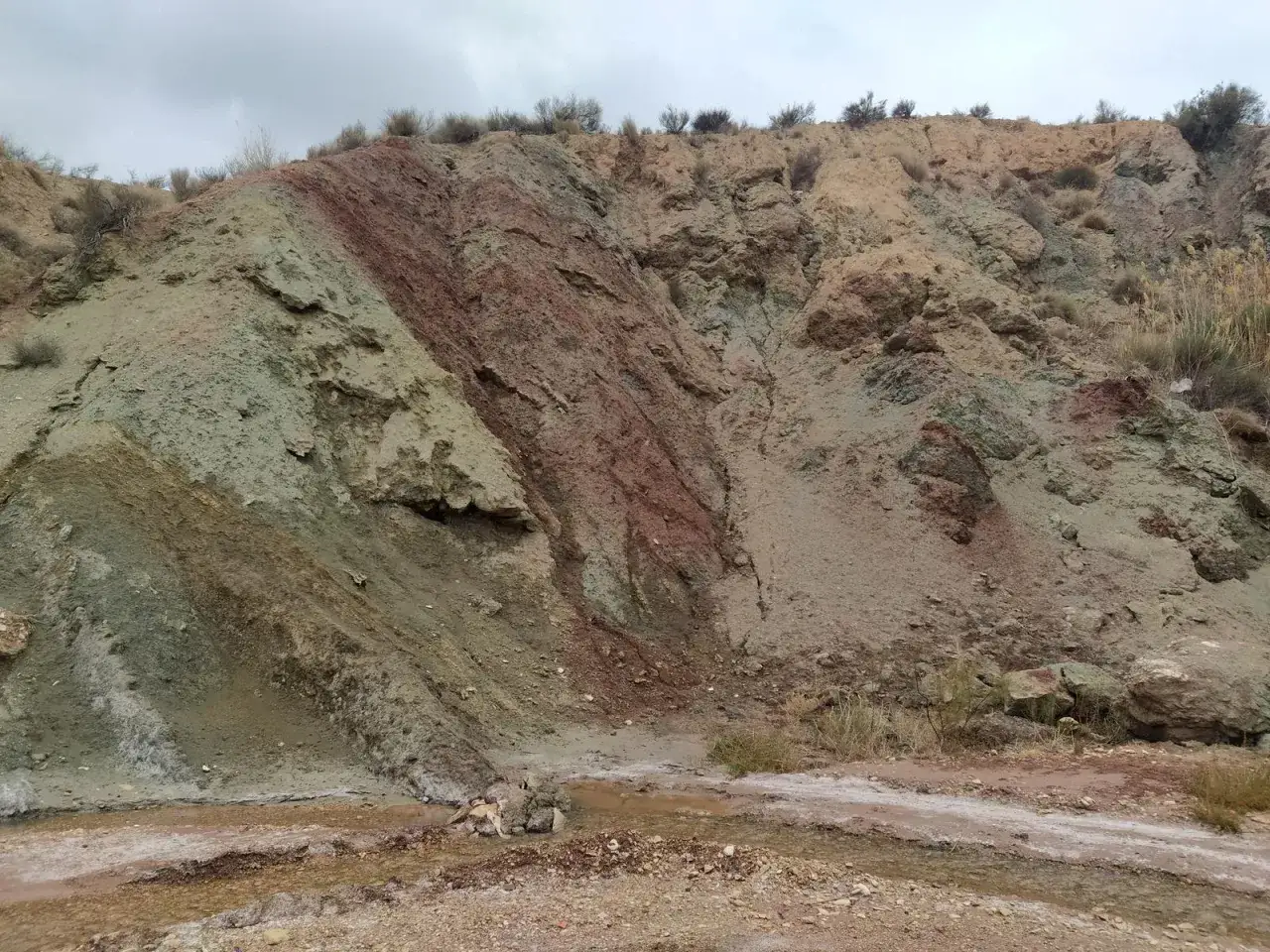 Terreno arcilloso con vetas verdes y rojizas en les salinetes de Novelda. Un peque&ntilde;o arroyo atraviesa el paisaje &aacute;rido.