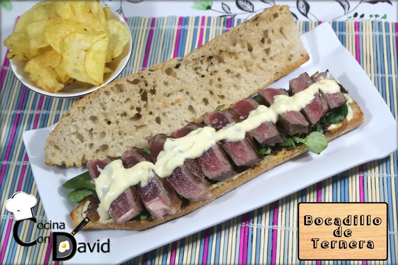 Bocadillo de ternera jugoso sobre pan r&uacute;stico, con patatas fritas al lado. &iexcl;Un manjar!