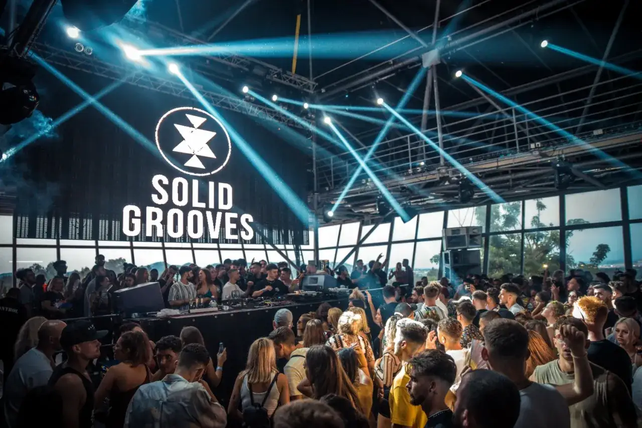 Multitud bailando bajo luces estroboscópicas en un club con el logo de Solid Grooves Ibiza en la pantalla.