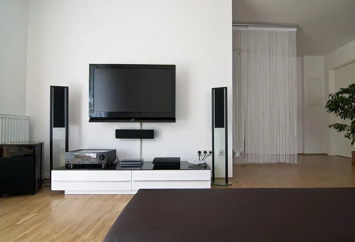 Salon moderne avec téléviseur fixé au mur sans voir les fils. Deux enceintes verticales flanquent l'écran.