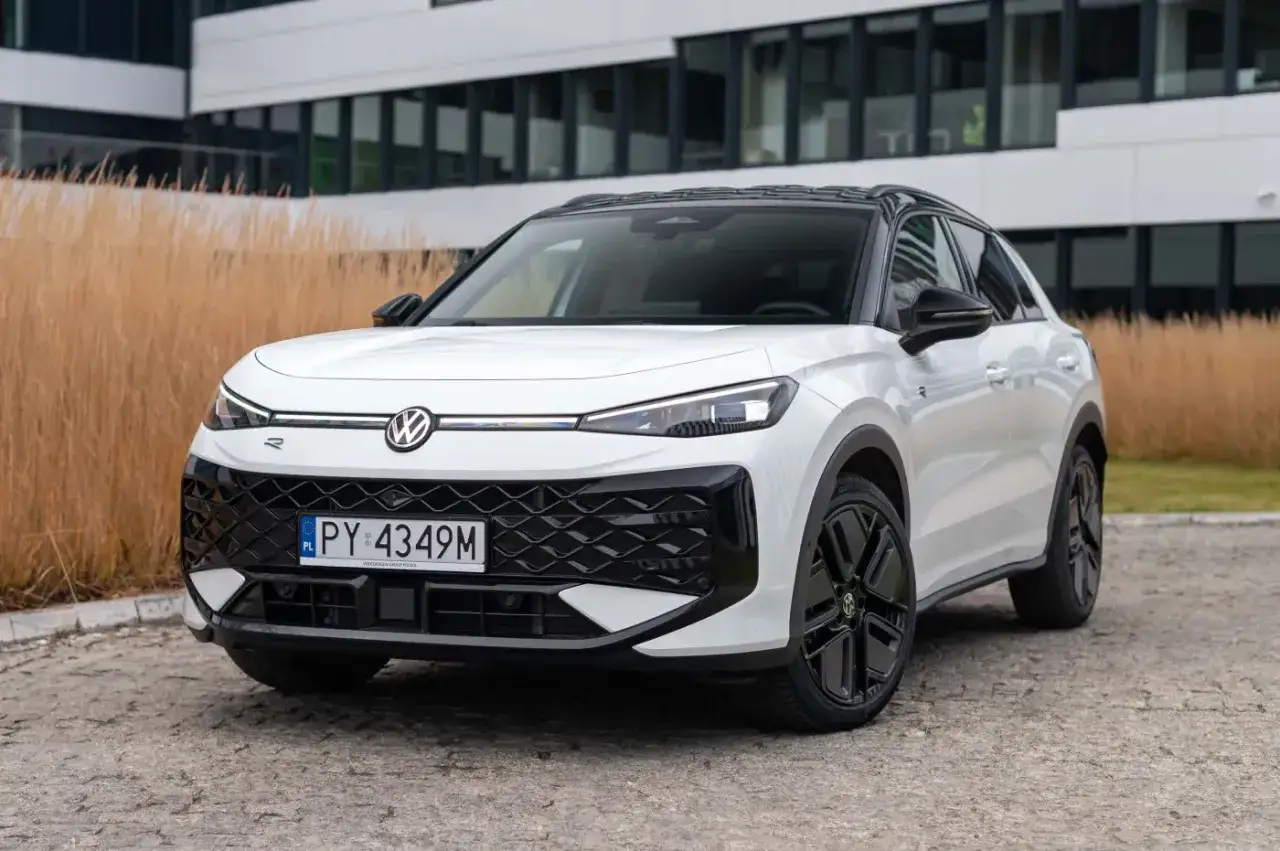 Biały Volkswagen ID.4 z czarnym dachem i felgami, jeden z nowoczesnych volkswagen modele, stoi na tle budynku i suchych traw.