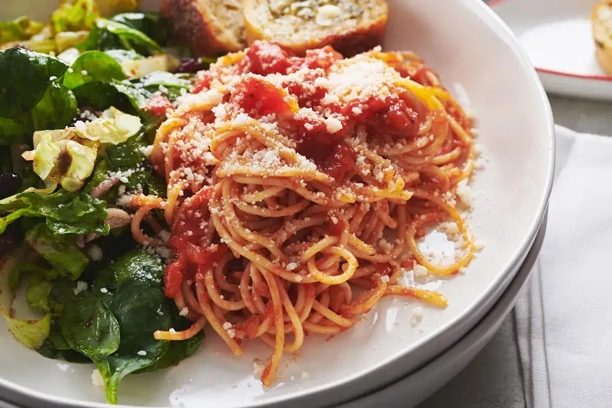 Porcja spaghetti z sosem pomidorowym i parmezanem, obok sałatka i pieczywo. Idealne na obiad, gdy liczymy spaghetti kcal.